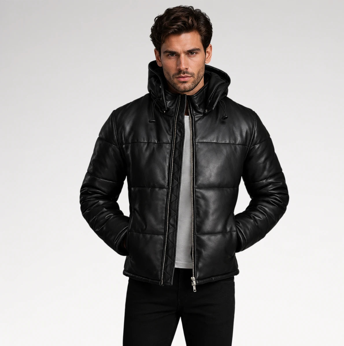 A man wearing a black quilted leather hooded jacket over a gray shirt and black pants, standing against a light gray studio background. Main image