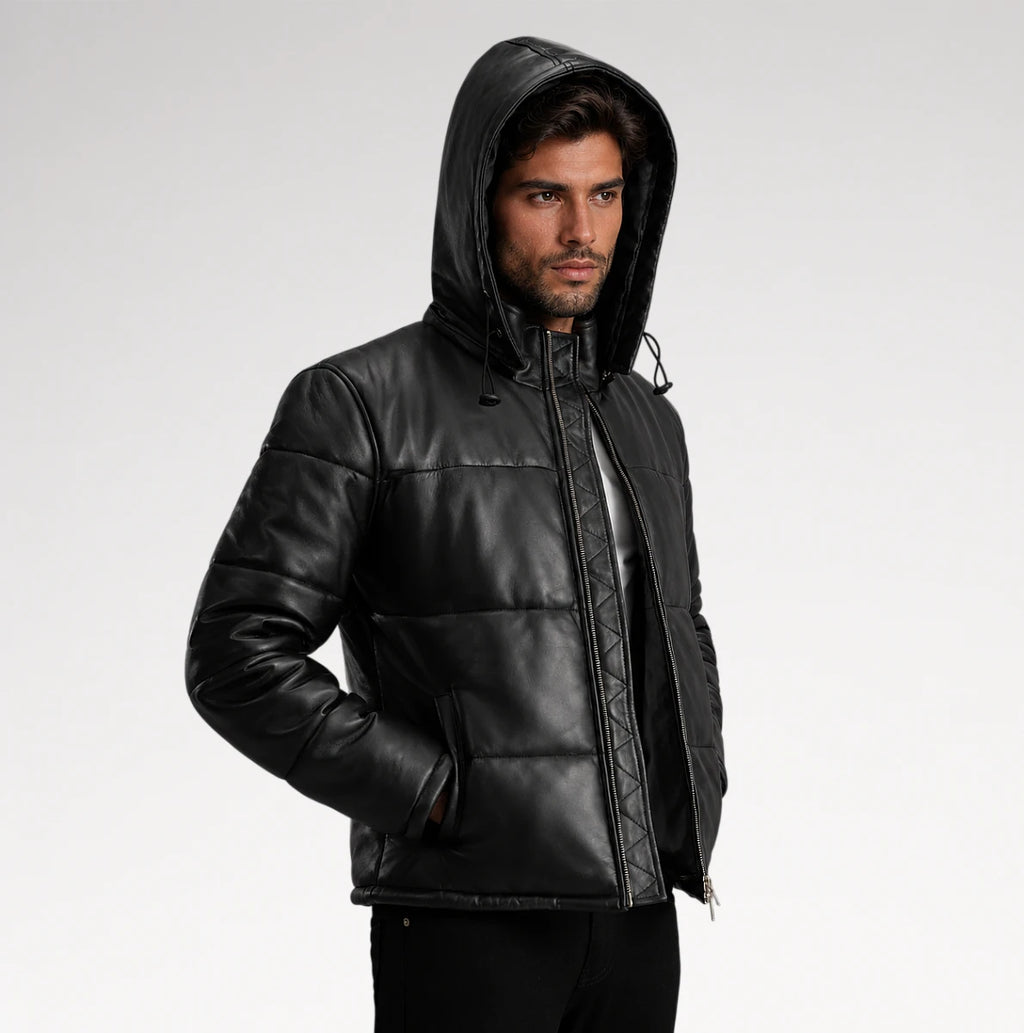 A man wearing a black hooded puffer jacket with quilted stitching, photographed against a plain light gray studio background.
