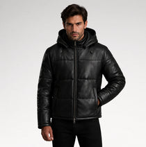 A man wearing a black leather hooded puffer jacket with a front zipper and horizontal quilted stitching, photographed against a light gray studio background.