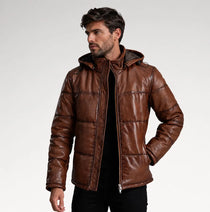 A man wearing a brown faux-leather hooded puffer jacket over a black shirt, photographed against a light gray studio background.