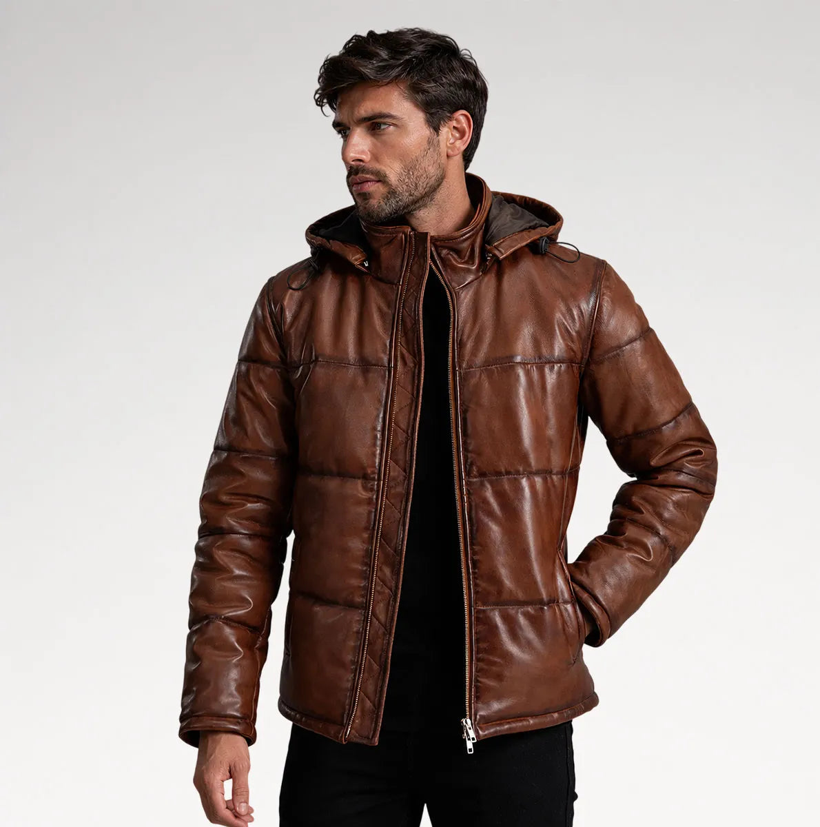 A man wearing a brown faux-leather hooded puffer jacket over a black shirt, photographed against a light gray studio background.
