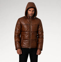 A man wearing a brown leather hooded puffer jacket with horizontal quilting, standing against a light gray studio background.