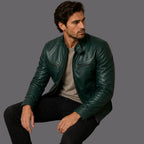 Man wearing a green leather jacket sitting on a brown chair against a gray background