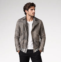 A man wearing a distressed gray faux-leather moto jacket over a white t-shirt and black pants, standing against a light gray studio background.