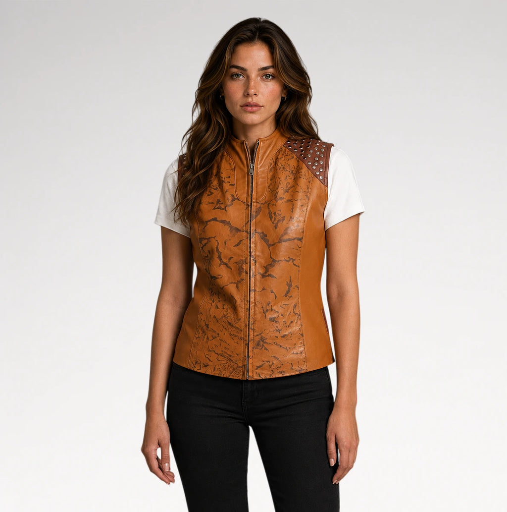 A woman modeling a sleeveless brown faux-leather vest with a black marble pattern, a front zipper, and studded shoulder details, worn over a white t-shirt and black pants against a light gray studio background.