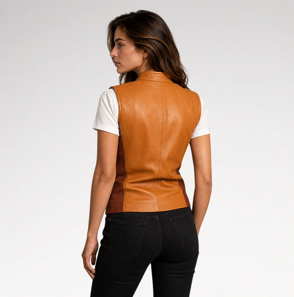 A woman shown from the back wearing a tan leather vest over a white short-sleeve top and black jeans, photographed against a light gray studio background.