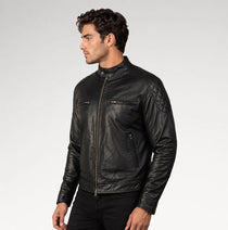 A man wearing a black leather motorcycle jacket with quilted shoulder detailing, shown in profile against a light gray studio background.