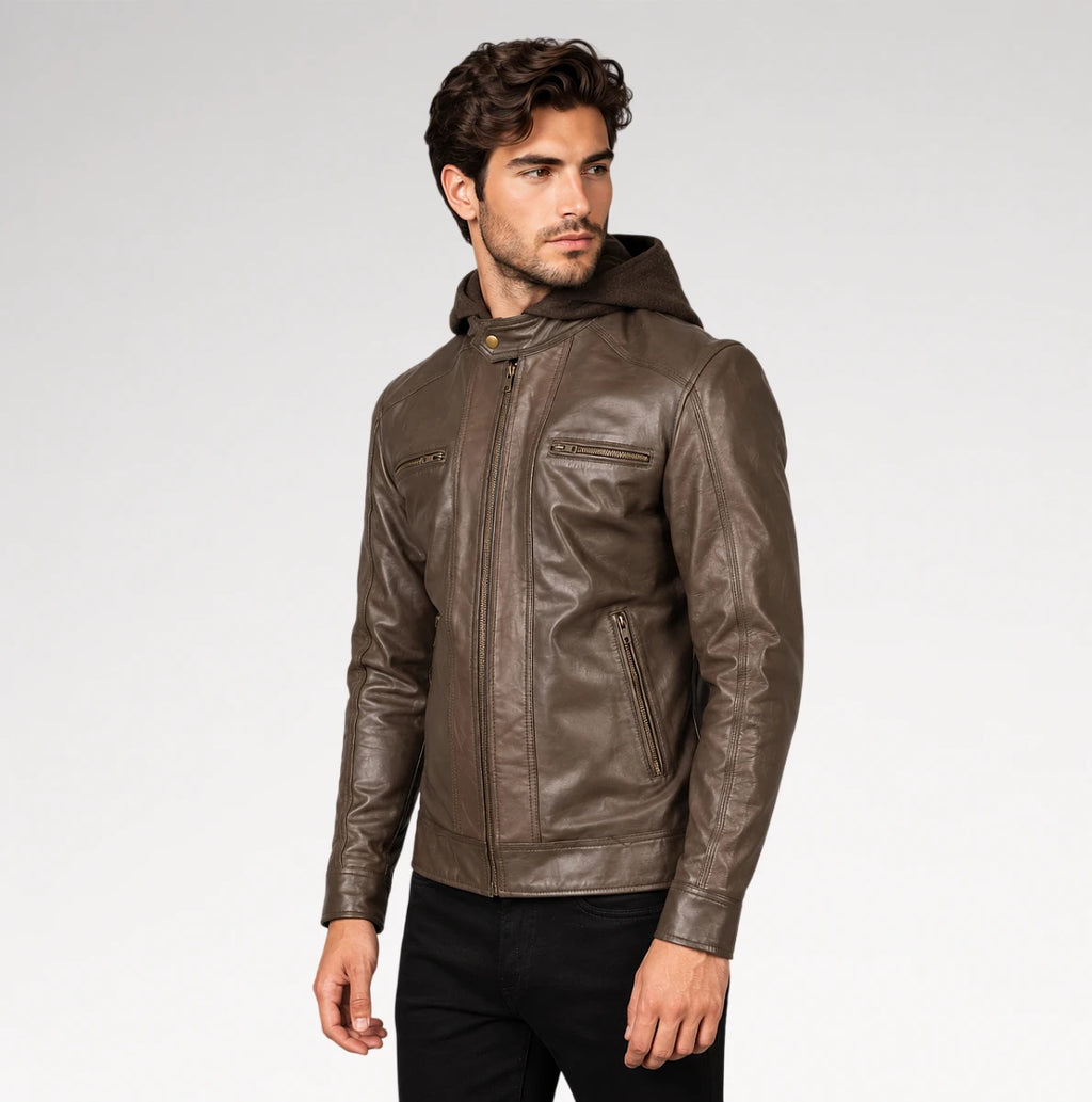 A man wearing a brown leather hooded jacket with zippered pockets, paired with black pants, photographed against a light gray studio background.