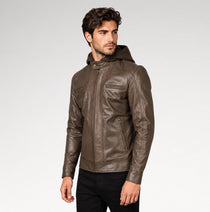 A man wearing a brown leather hooded jacket with zippered pockets, paired with black pants, photographed against a light gray studio background.