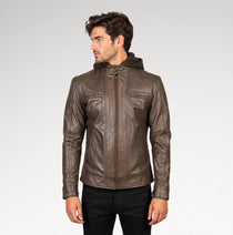 A man wearing a brown leather hooded jacket with zippered chest pockets, shown from the waist up against a light gray studio background.