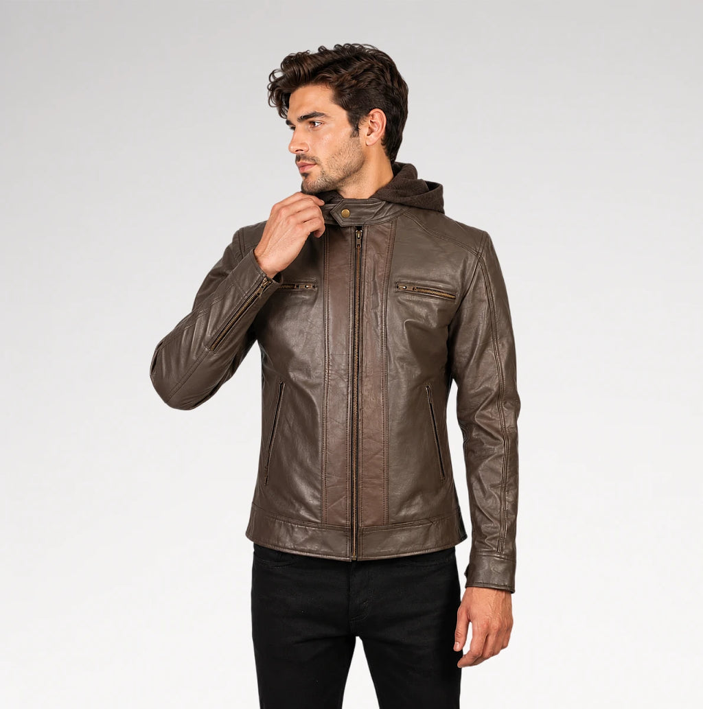A man wearing a brown faux-leather hooded jacket with zippered chest pockets, paired with black pants, photographed against a light gray studio background.