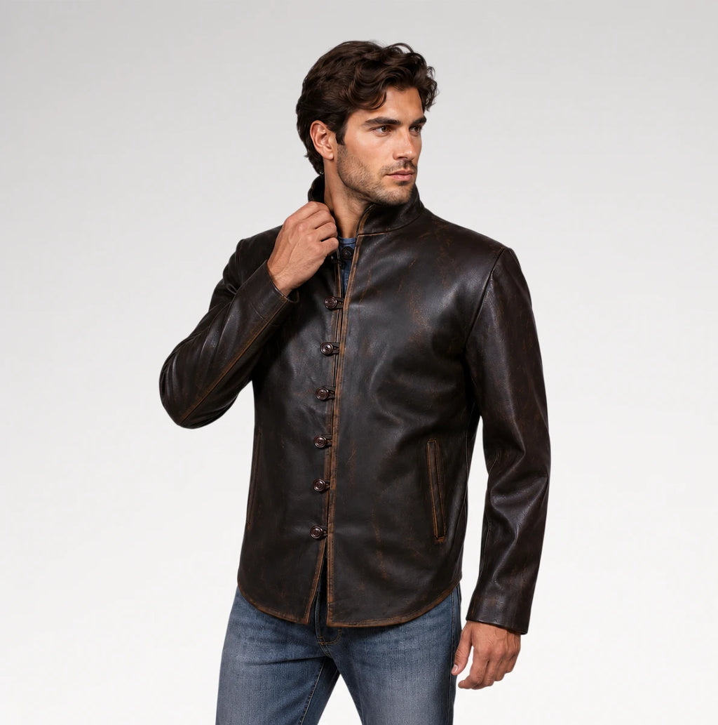 A man wearing a dark brown leather jacket with a mandarin collar and button closure, paired with blue jeans, photographed against a light gray studio background.