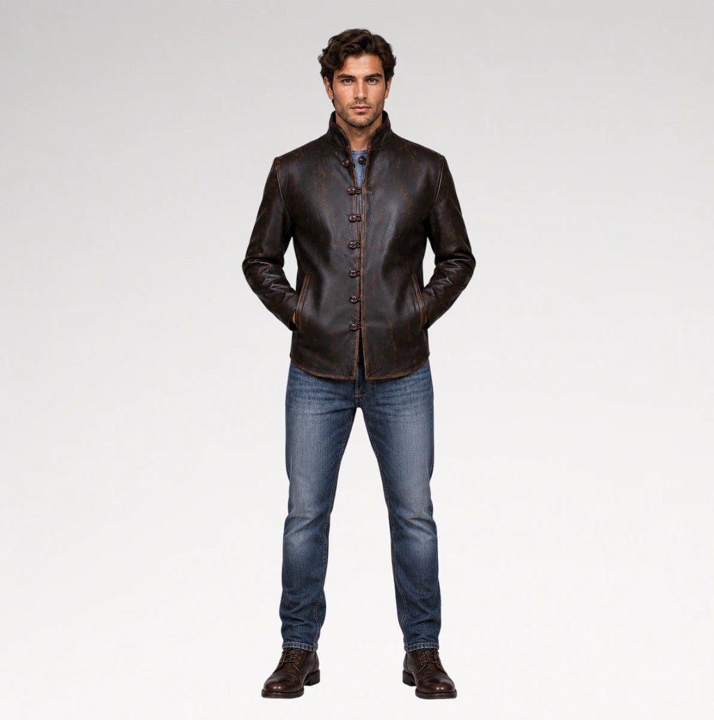 A man modeling a dark brown leather jacket with a stand collar and button front, paired with blue jeans and brown leather shoes, against a light gray studio background.