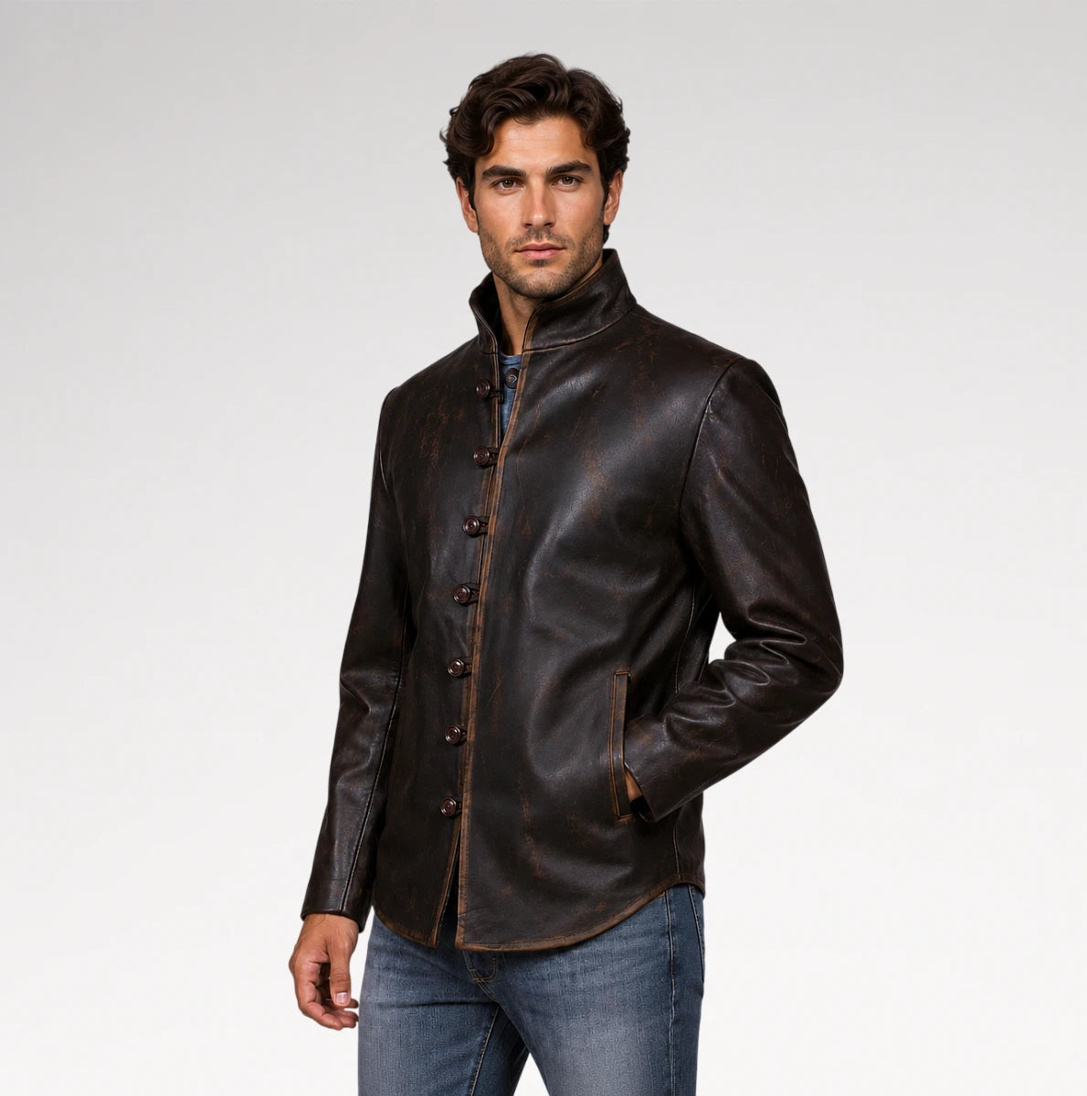 A man wearing a dark brown leather jacket with a high stand-up collar and decorative front buttons, paired with blue jeans, photographed against a light gray studio background.