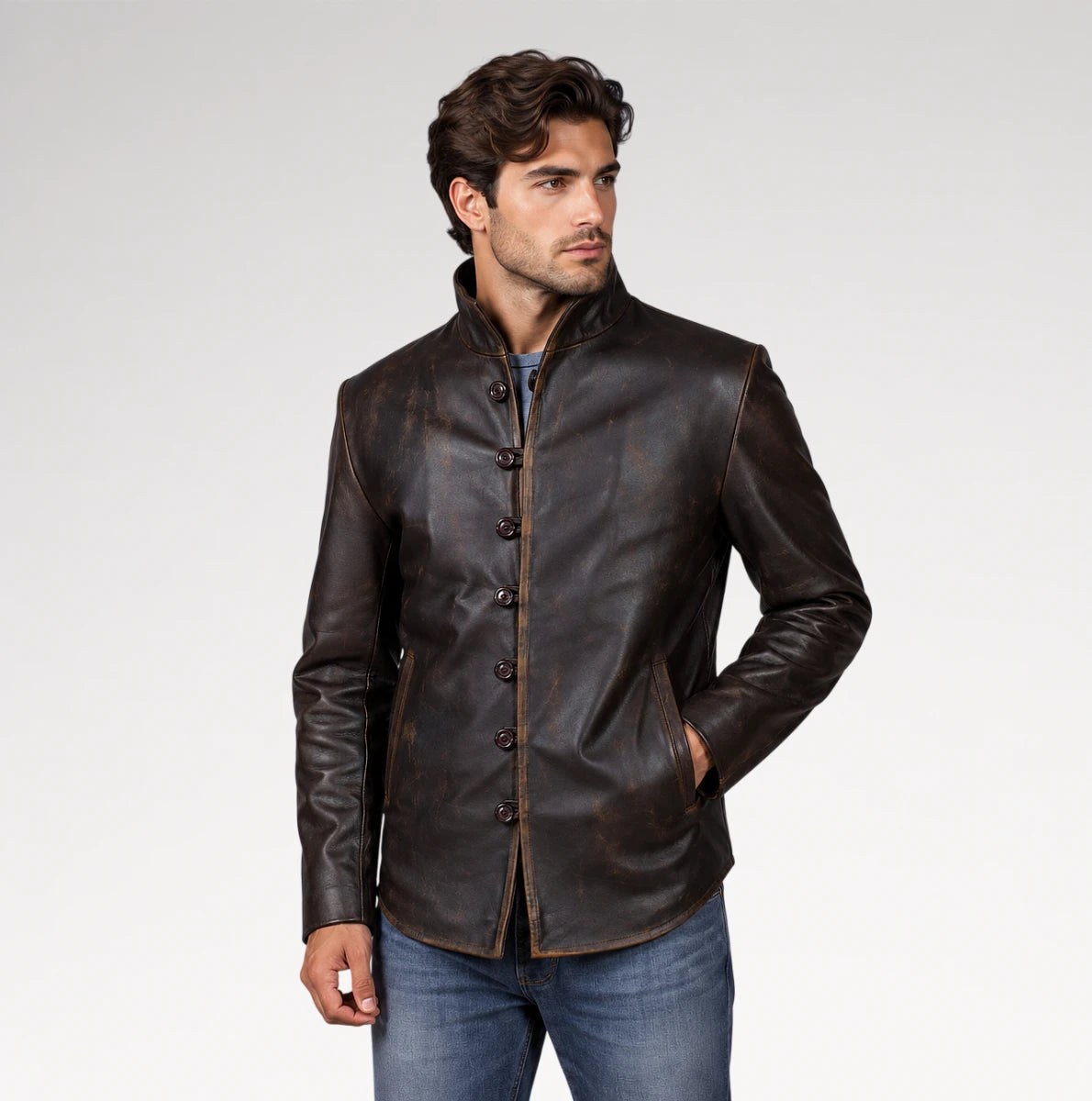 A man wearing a dark brown leather jacket with a mandarin collar and button closure, paired with blue jeans, photographed against a light gray studio background.