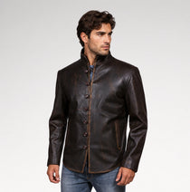 A man wearing a dark brown leather jacket with a mandarin collar and button front, paired with blue jeans, photographed against a light gray studio background.