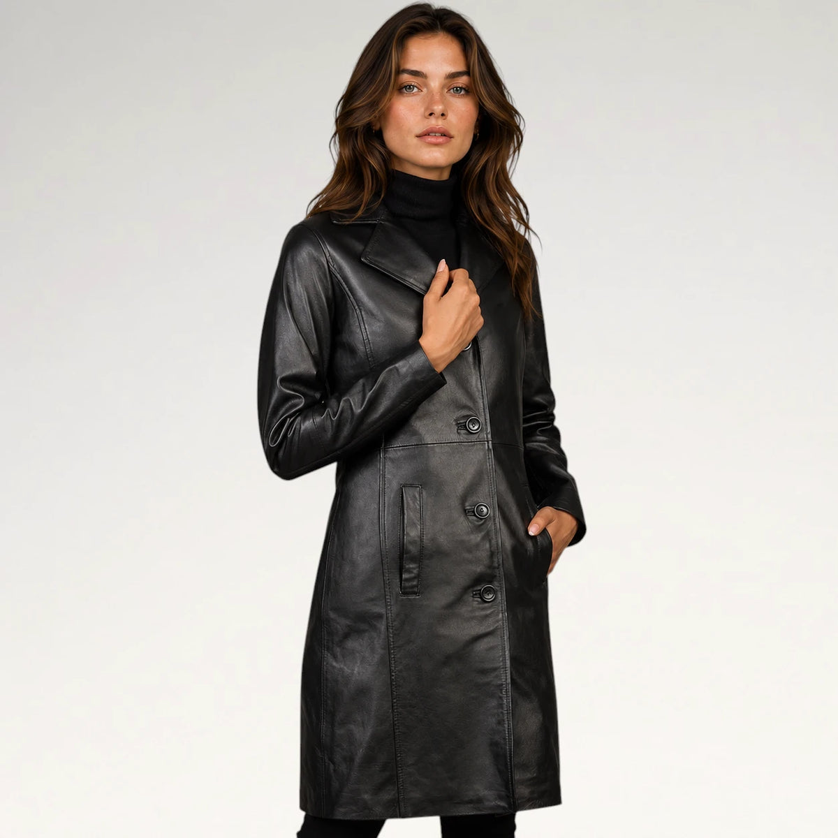 A woman modeling a black faux-leather double-breasted coat over a black turtleneck, photographed against a light gray studio background.