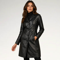A woman modeling a black faux-leather double-breasted coat over a black turtleneck, photographed against a clean white studio background.