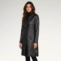 A woman modeling a black leather coat over a black turtleneck sweater, photographed against a clean light gray studio background.