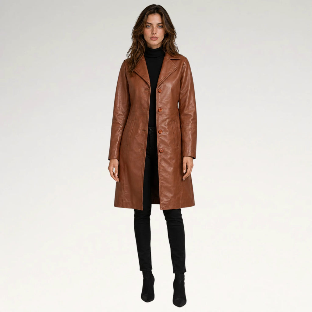A woman modeling a mid-length brown faux-leather coat over a black turtleneck, black pants, and black ankle boots, photographed against a seamless light gray studio background.