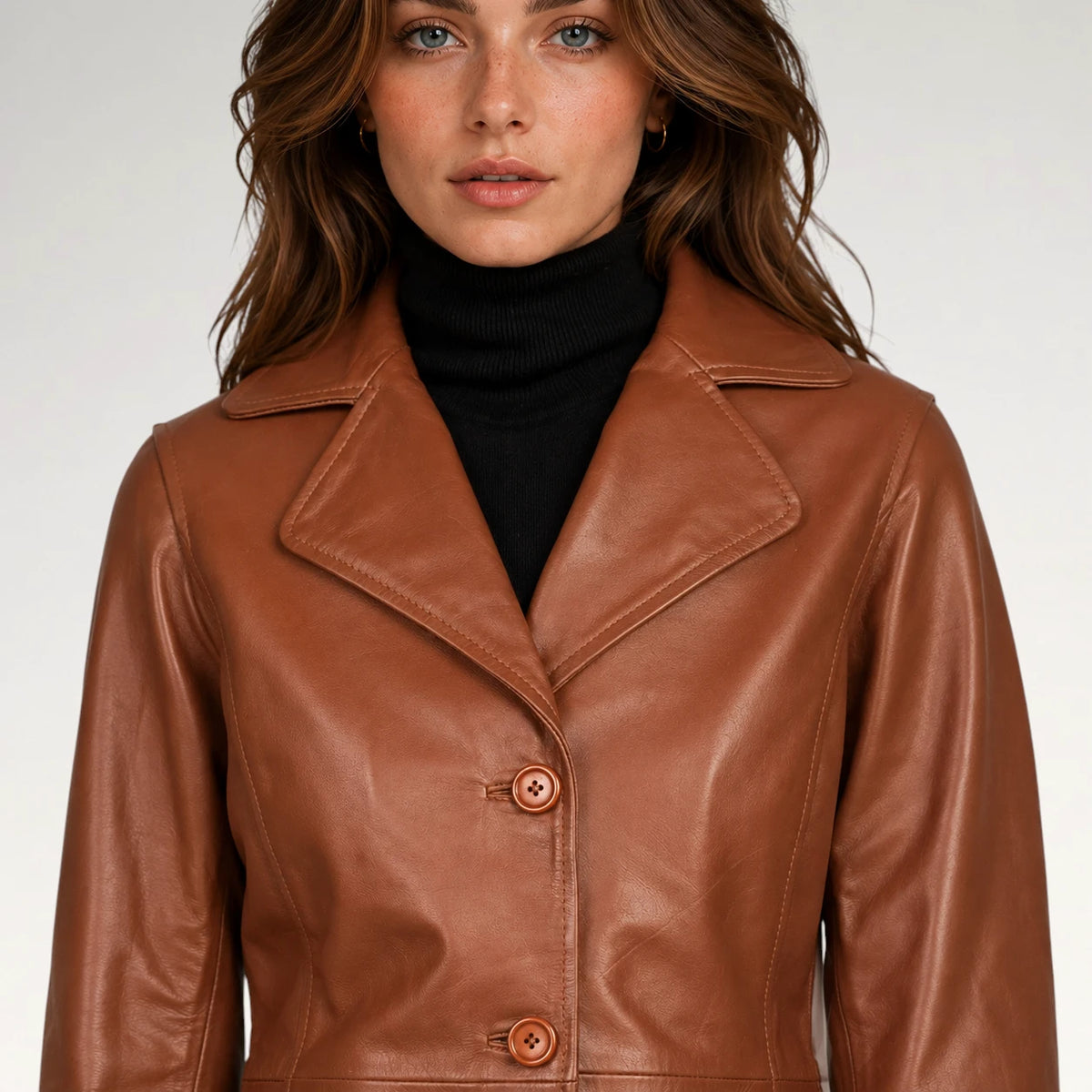 A woman wearing a brown leather jacket over a black turtleneck sweater, photographed against a plain light gray studio background.