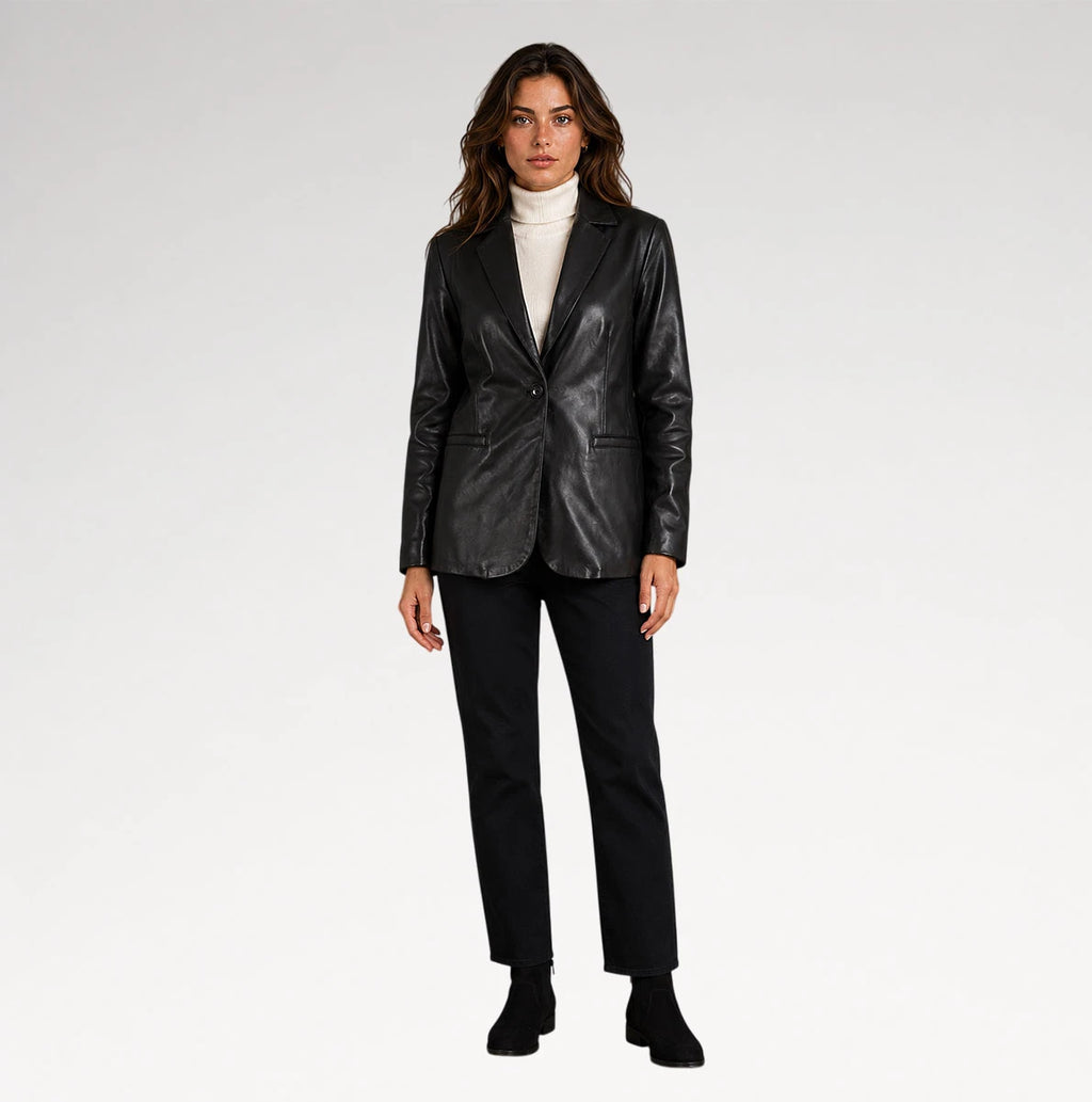 A woman modeling a black leather blazer over a white turtleneck sweater, paired with black trousers and black ankle boots, against a plain light gray studio background.