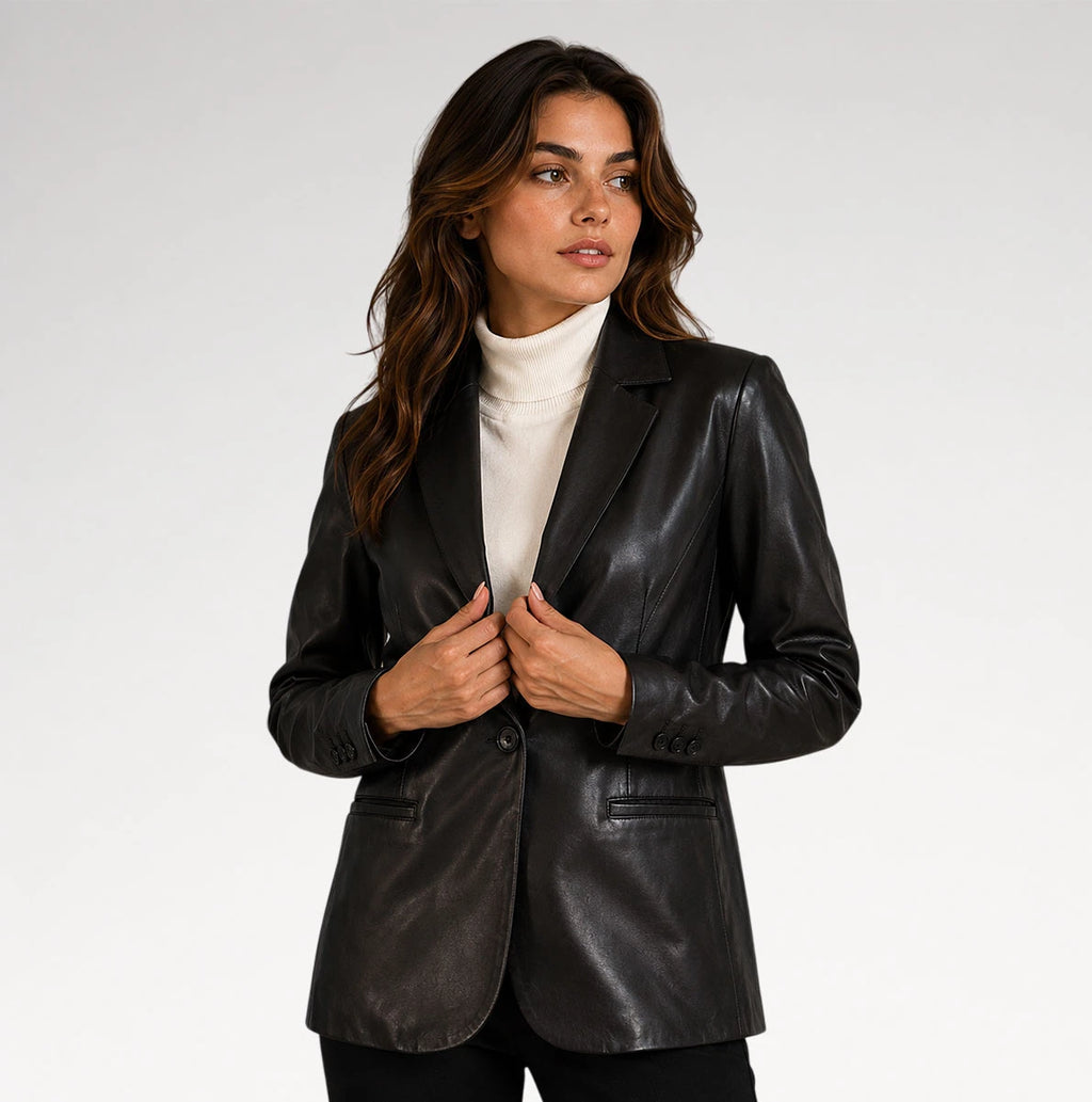 A woman wearing a black leather blazer over a white turtleneck sweater, photographed against a plain light gray studio background.