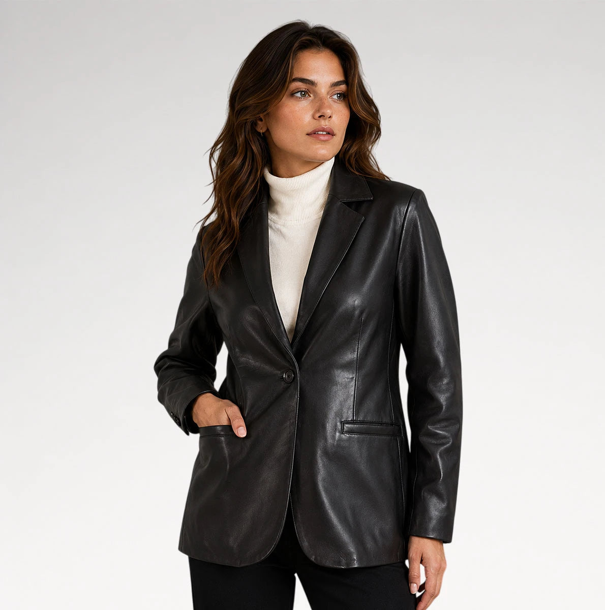 A woman wearing a black faux-leather blazer over a cream turtleneck sweater and black pants, photographed against a plain light gray studio background. Main image