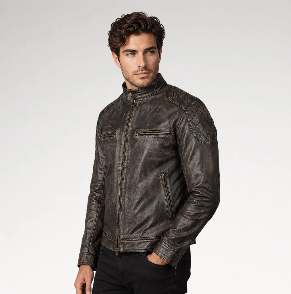 A man wearing a dark brown distressed leather motorcycle jacket, standing against a light gray studio background.