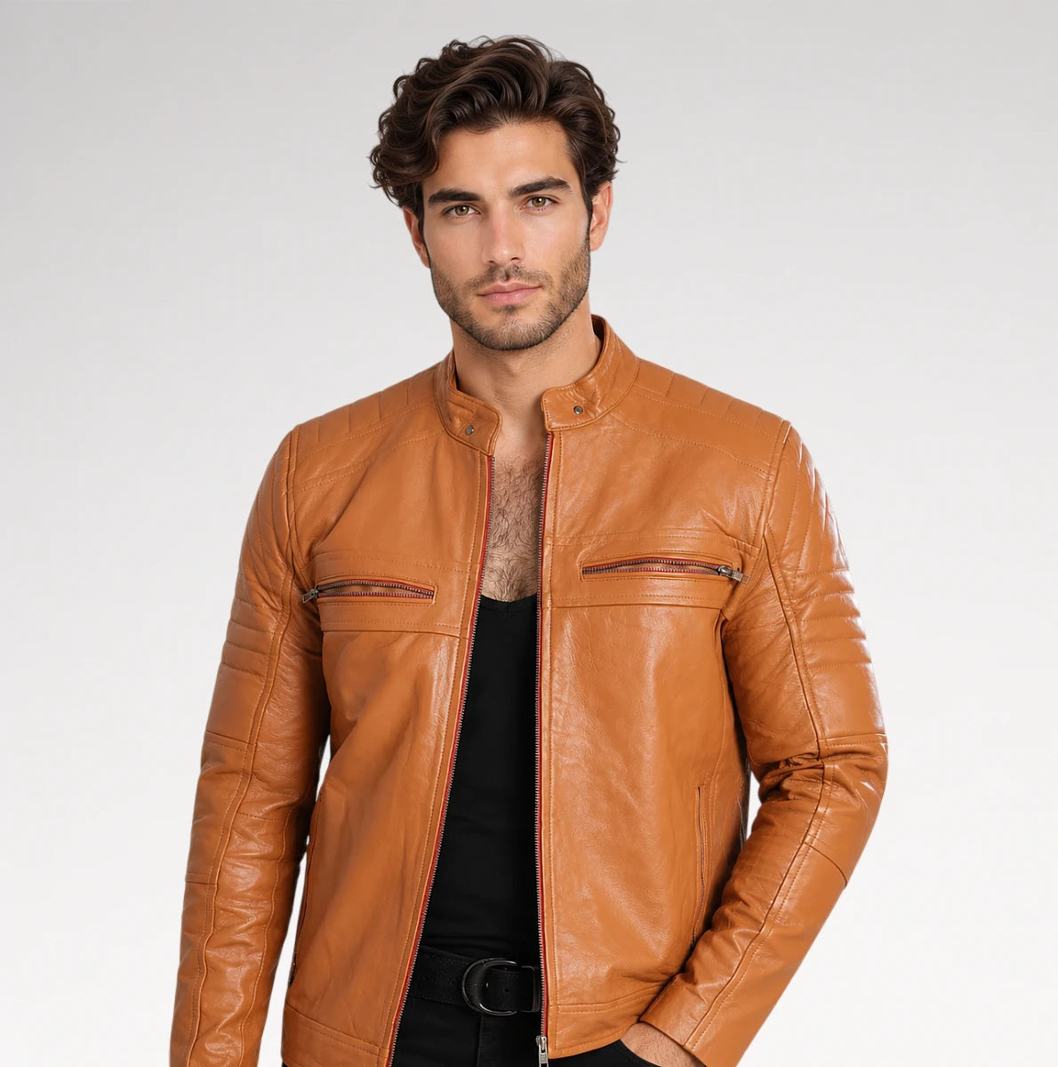 A man wearing a tan leather motorcycle jacket over a black shirt, photographed against a light gray studio background.