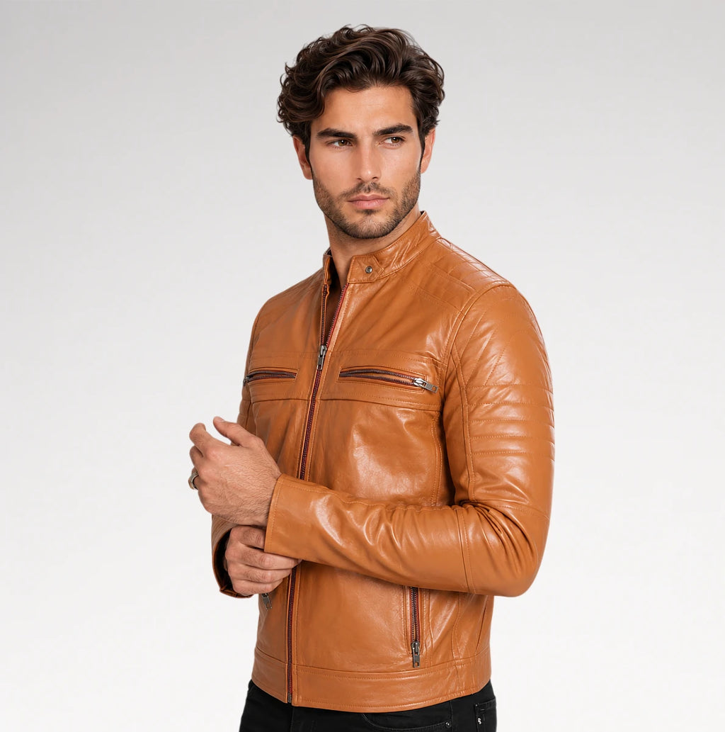 A man wearing a tan leather motorcycle jacket, standing against a light gray studio background.