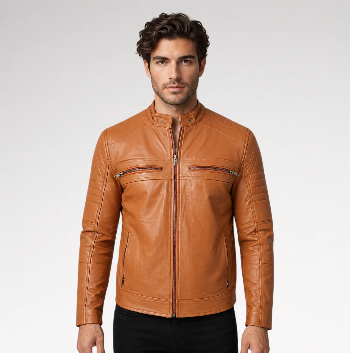A man wearing a tan leather moto jacket with a front zipper and zippered chest pockets, paired with black pants, against a light gray studio background. Main image