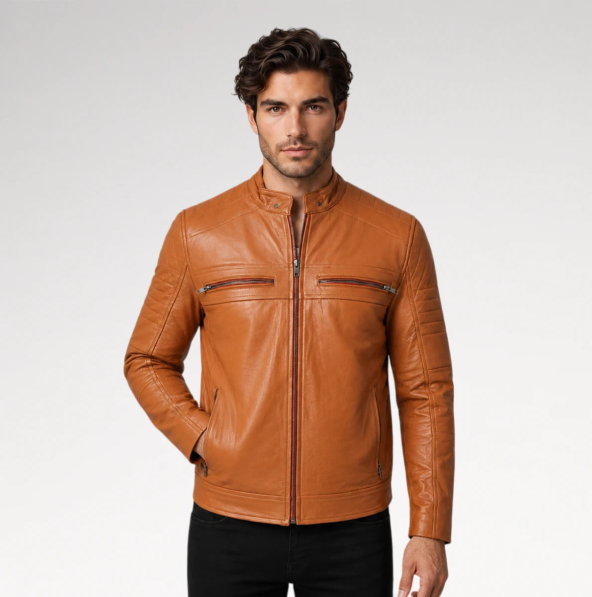 A man wearing a tan leather jacket with a stand collar, front zipper, and zippered chest pockets, paired with black pants, photographed against a light gray studio background.