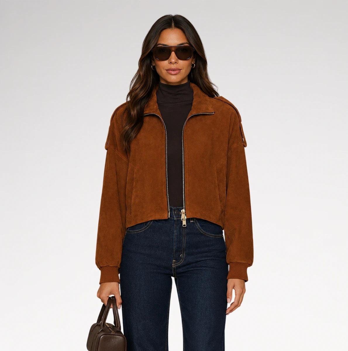 A woman modeling a cropped brown suede jacket over a black turtleneck, paired with dark blue jeans and holding a brown handbag, set against a plain light gray studio background. Main image