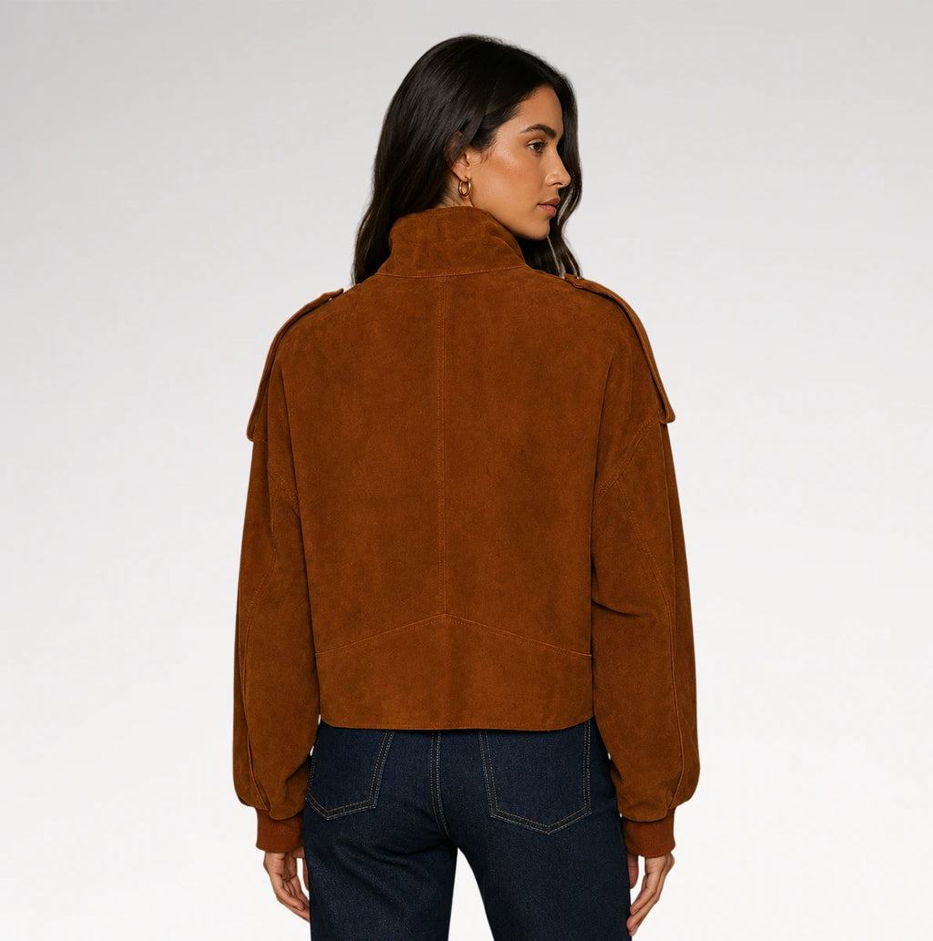 A woman shown from the back wearing a cropped brown suede jacket with shoulder epaulets, paired with dark blue jeans, against a light gray studio background.