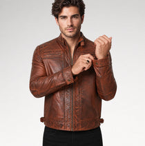 A man wearing a brown distressed leather jacket with a stand collar, zippered front, and contrast stitching, posed against a light gray studio background.