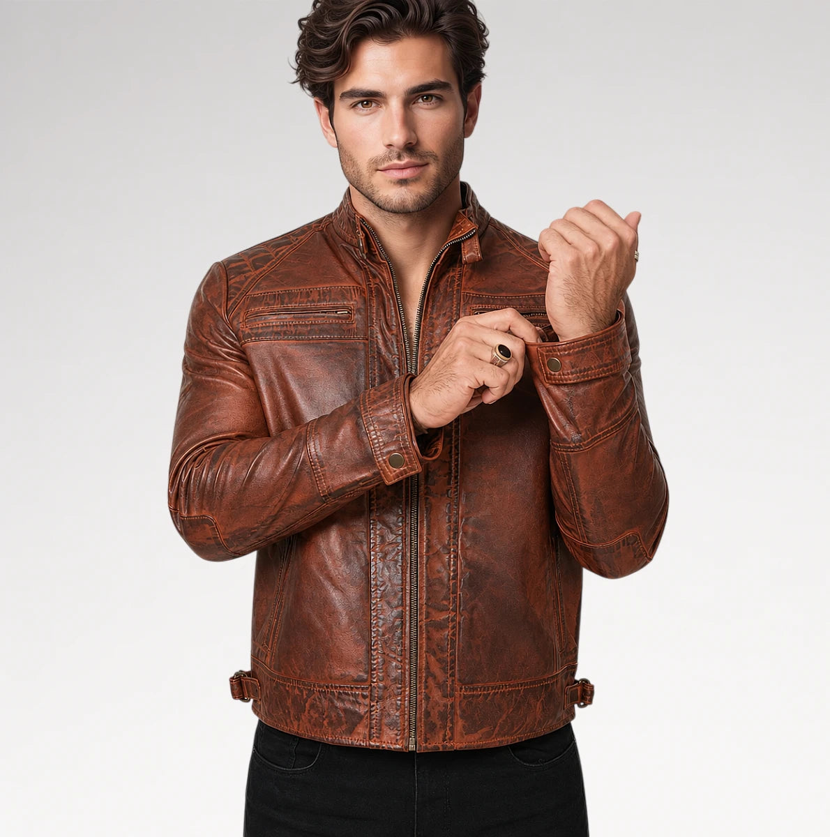 A man wearing a brown distressed leather jacket with a stand collar, zippered front, and contrast stitching, posed against a light gray studio background.