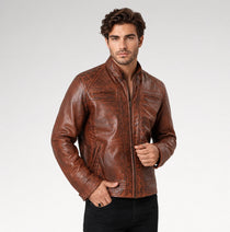 A man wearing a brown distressed leather jacket with a stand-up collar and zippered front, paired with black pants, photographed against a light gray studio background.