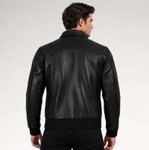 A man viewed from the back wearing a black leather jacket with ribbed knit collar, cuffs, and hem, set against a plain light gray studio background.