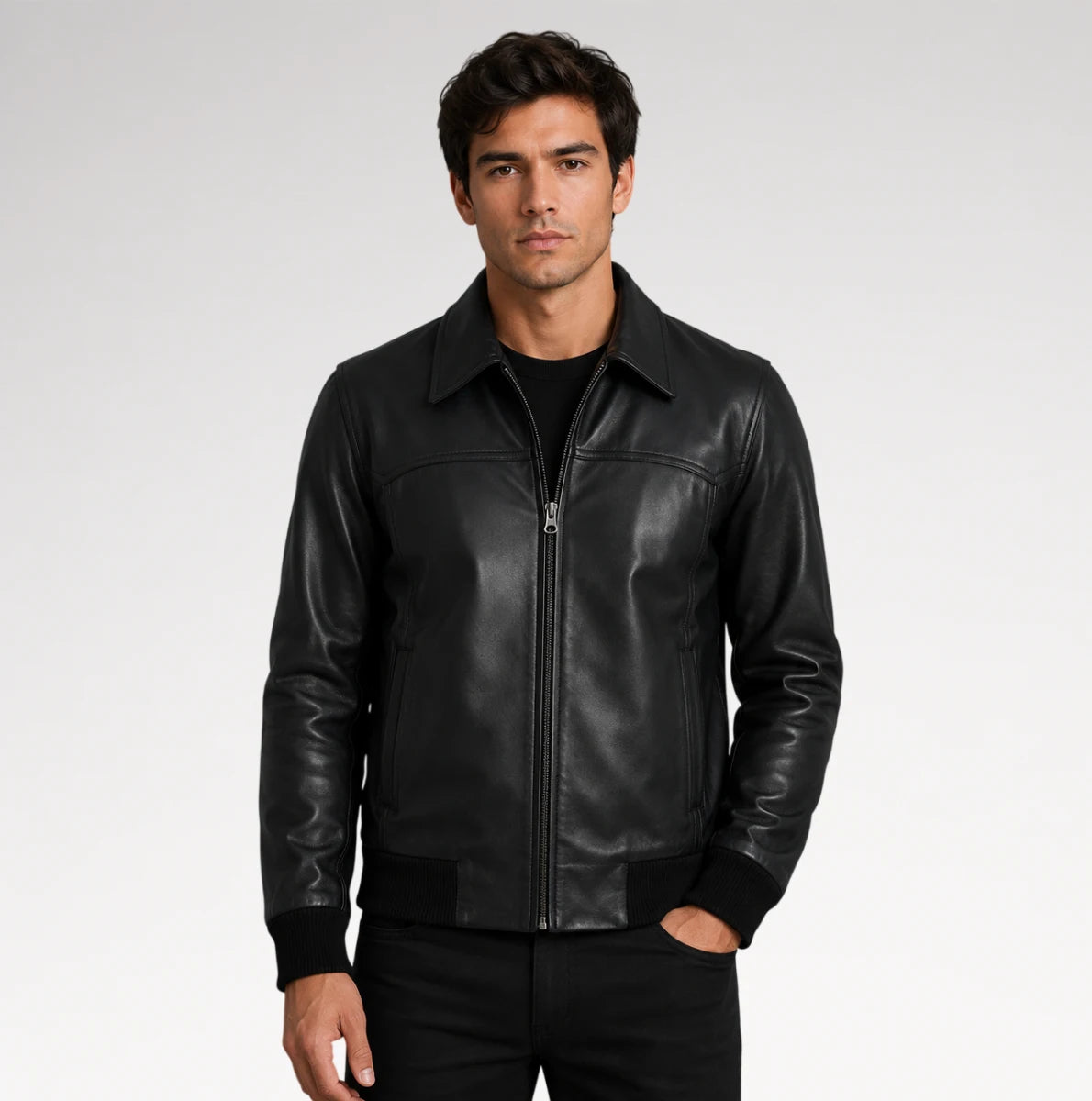 A man wearing a black leather jacket with a front zipper, ribbed collar, cuffs, and hem, paired with a black t-shirt and black pants, photographed against a light gray studio background. Main image