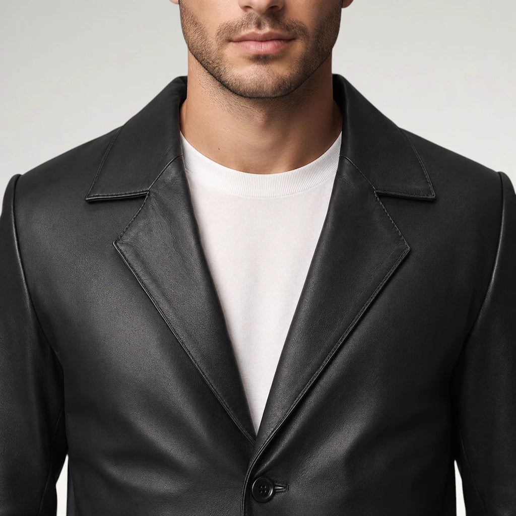 A close-up of a man wearing a black leather blazer over a white crewneck t-shirt, cropped from the chin down against a light gray studio background.