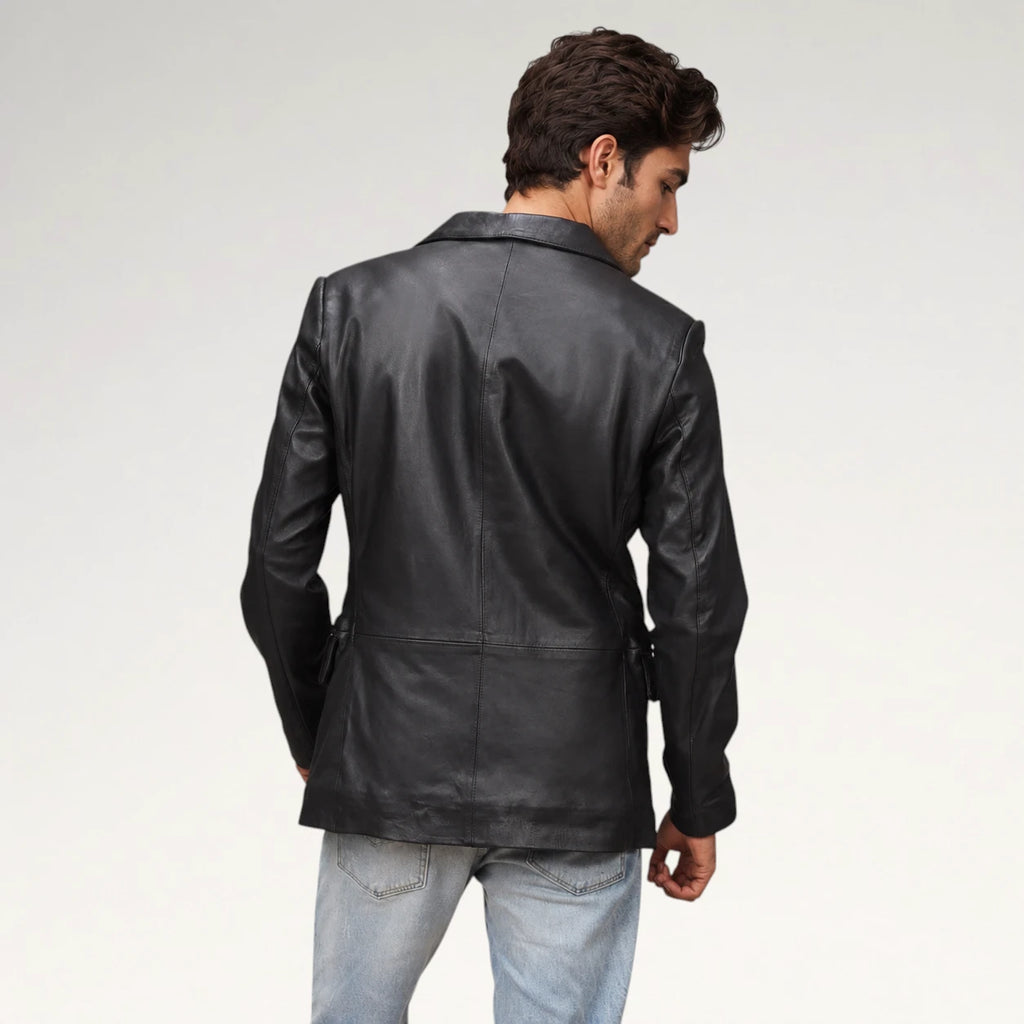 A man wearing a black leather blazer, shown from the back and side, paired with light blue jeans against a plain light gray studio background.