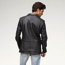 A man wearing a black leather blazer, shown from the back and side, paired with light blue jeans against a plain light gray studio background.
