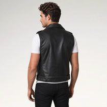 A man wearing a black leather vest over a white t-shirt and black pants, shown from the back against a light gray studio background.
