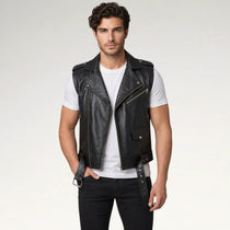 A man modeling a black leather biker vest over a white t-shirt and black jeans, standing against a light gray studio background.