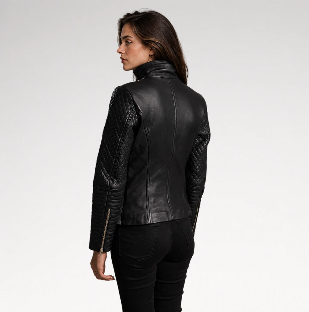 A woman shown from the back wearing a black leather jacket with quilted sleeves and a high collar, paired with black pants, against a plain light gray studio background.