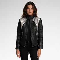 A woman modeling a black quilted leather jacket with metallic silver shoulder panels, styled with a black top and black pants against a light gray studio background.