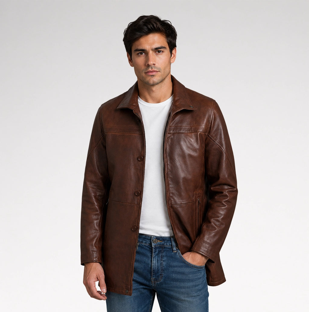 A man wearing a brown leather jacket over a white t-shirt and blue jeans, standing against a light gray studio background.