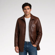 A man wearing a brown leather jacket over a white t-shirt and blue jeans, standing against a light gray studio background.