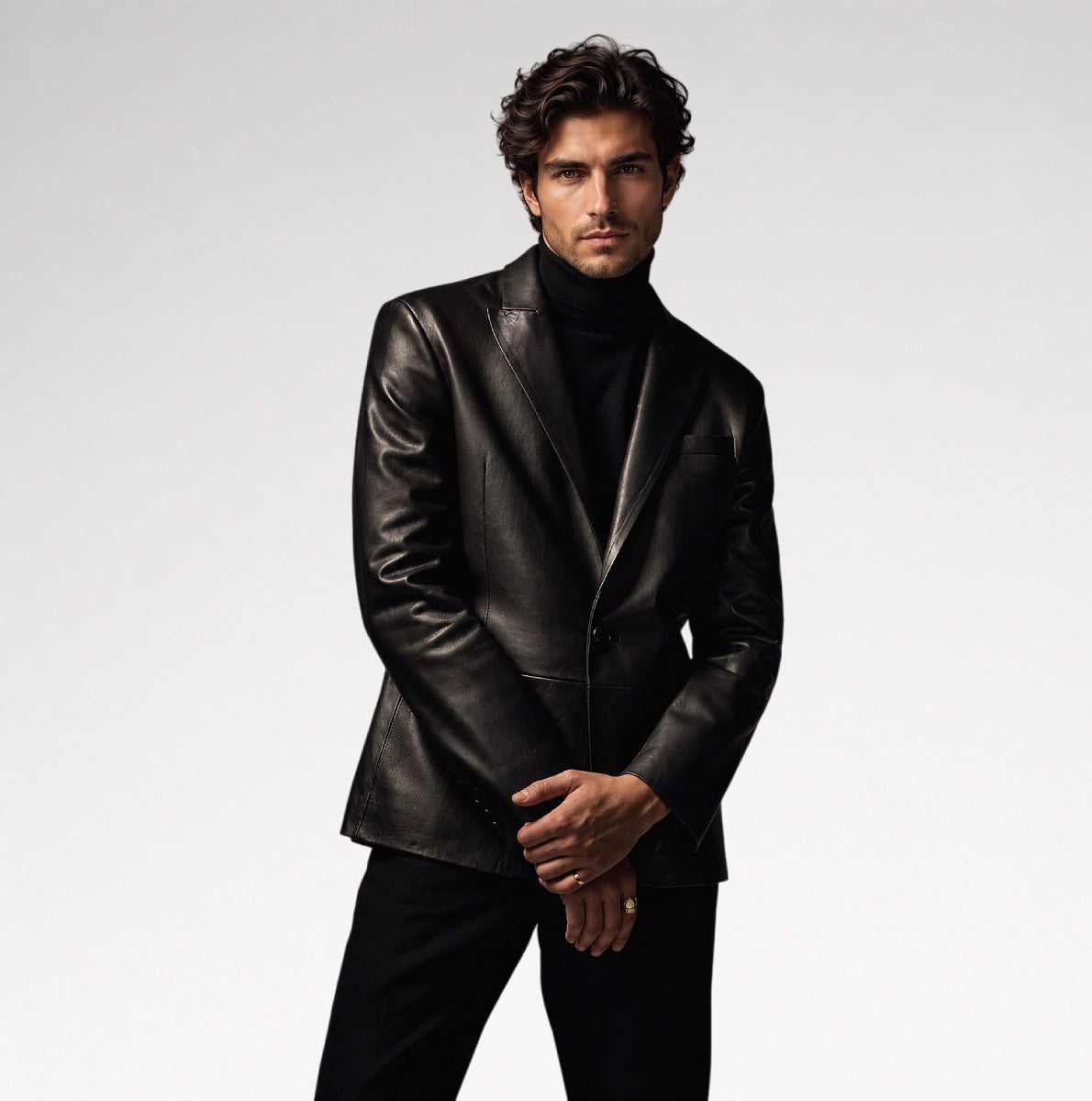 A man wearing a black leather blazer over a black turtleneck sweater and black trousers, standing against a light gray studio background. Main image